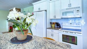 Une cuisine avec des meubles blancs, un four à micro-ondes, une cuisinière et une orchidée en pot posée sur le comptoir.