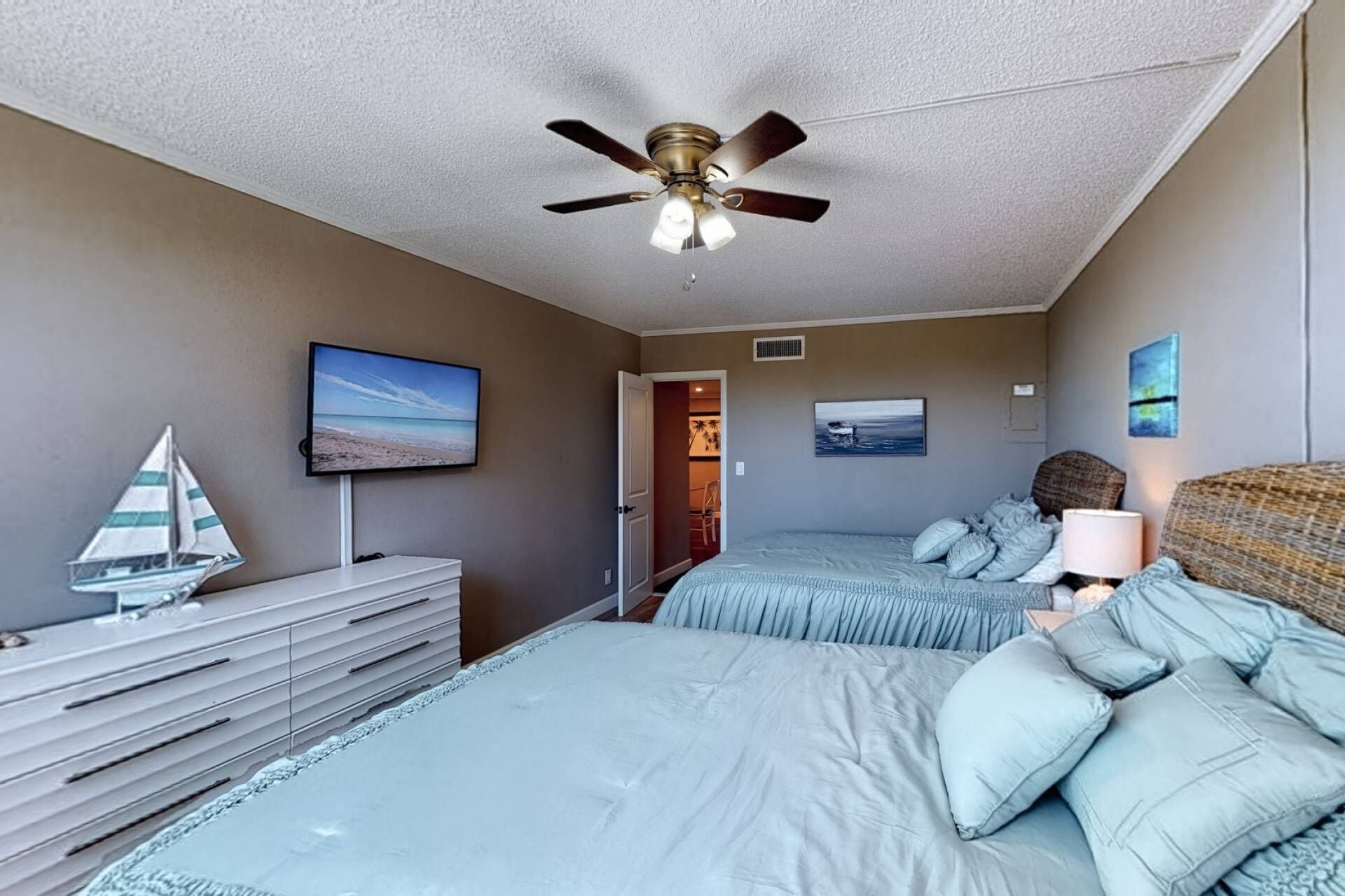Un dormitorio con dos camas, ventilador de techo, televisor y cómoda.