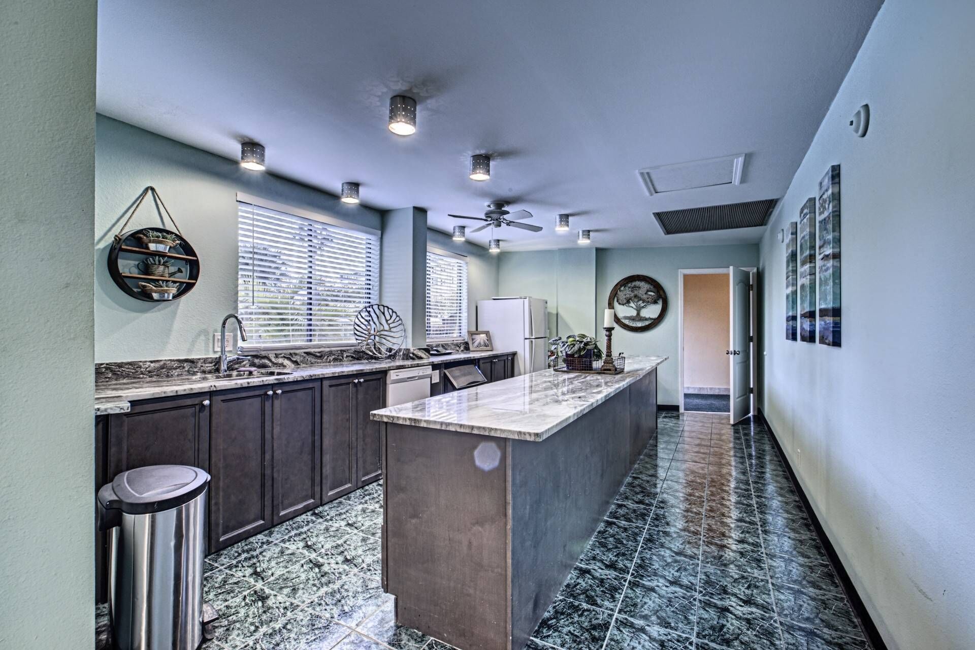 A modern kitchen with dark cabinets, a marble countertop, and a central island. There are ceiling lights and a ceiling fan.