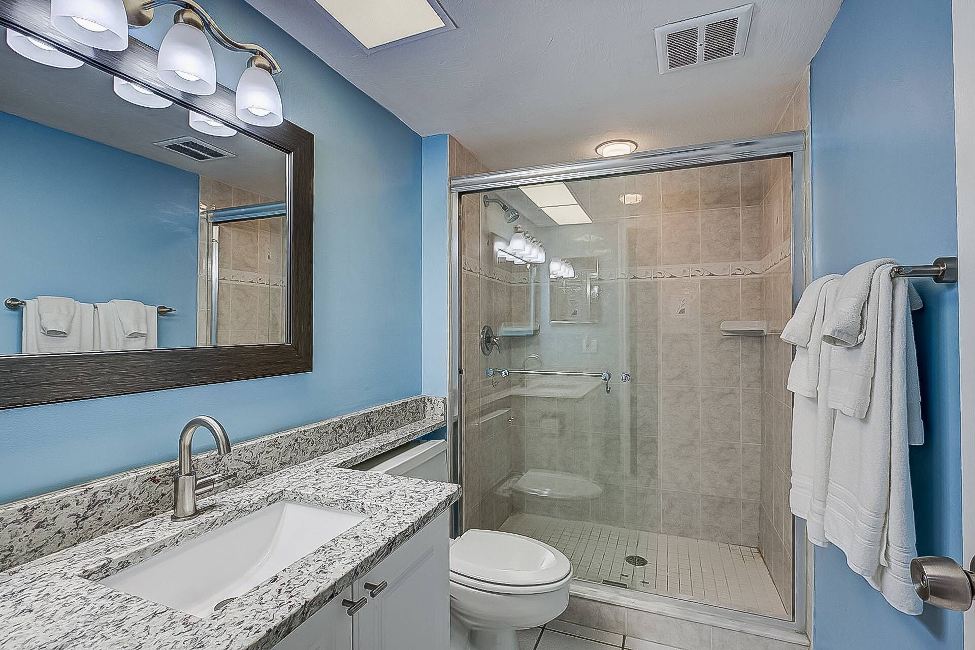 A bathroom with a glass-enclosed shower, a sink with a marble countertop, and a toilet.