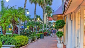 A pedestrian walkway lined with palm trees and planters, leading to a building with a red roof.