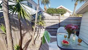 A patio with a glass table, chairs, and a small garden area with plants and a wooden fence.