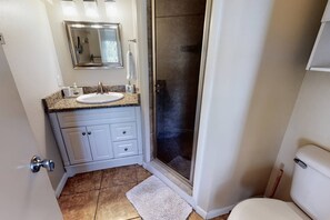 Un baño con lavamanos blanco, espejo, cabina de ducha y retrete.