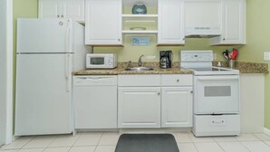Eine kleine Küche mit weißen Schränken, einer Mikrowelle, einer Kaffeemaschine, einem Geschirrspüler und einem Backofen.