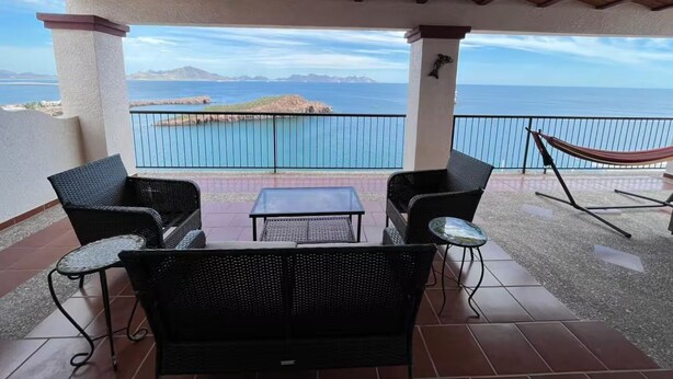 An outdoor patio with wicker furniture, a hammock, and a view of the ocean.