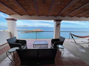 An outdoor patio with wicker furniture, a hammock, and a view of the ocean. - Stunning Panoramic Ocean Views – 4BR House at Caracol Peninsula (San Carlos)