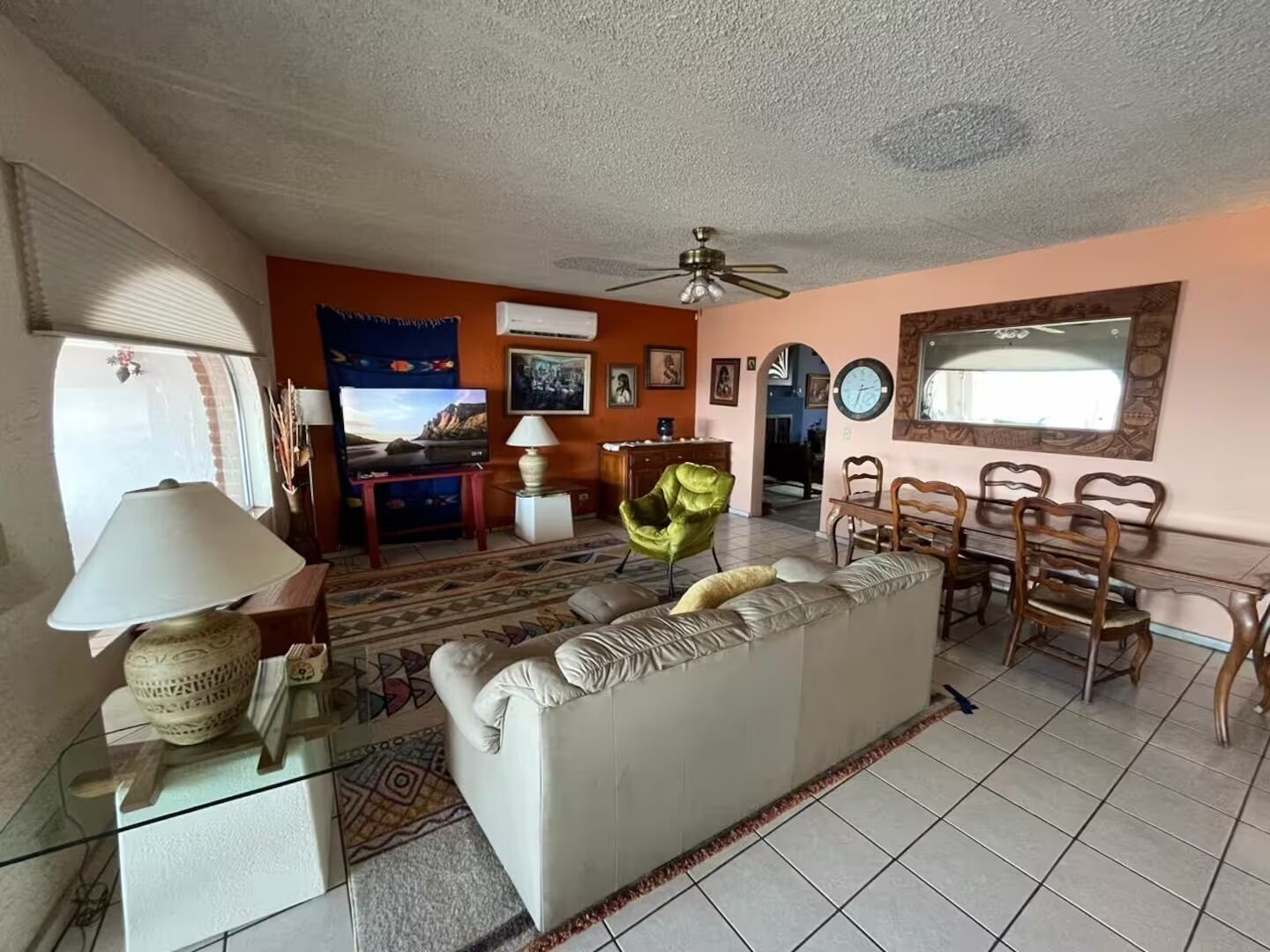 A living room with a sofa, a dining table with chairs, a television, and a ceiling fan.
