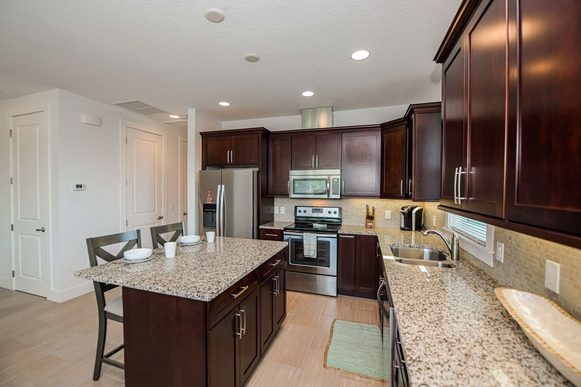 A modern kitchen with dark wood cabinets, stainless steel appliances, granite countertops, and a central island with seating.