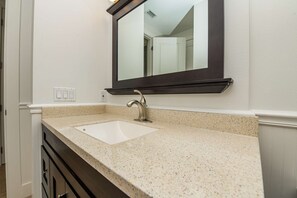 A bathroom with a white sink, a dark countertop, and a mirror above the sink.