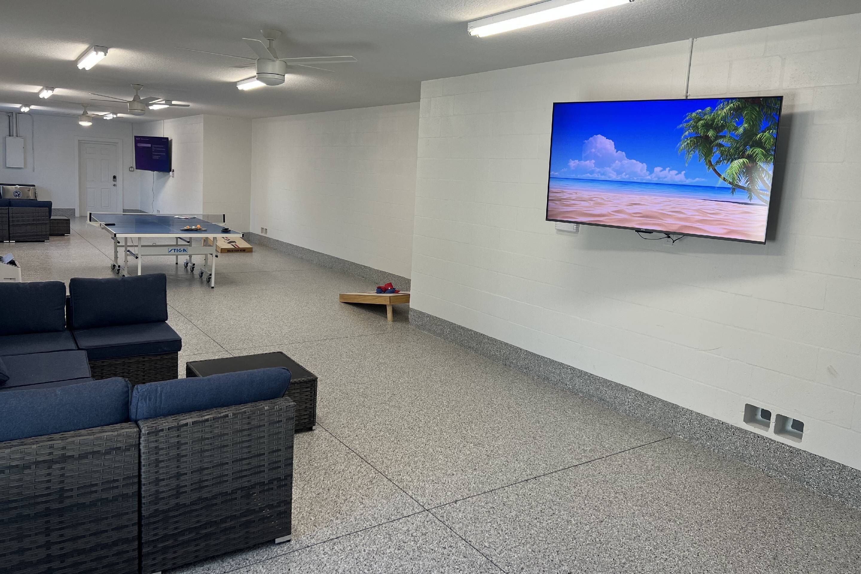 A spacious room with a ping pong table, a large flat-screen TV on the wall, and a comfortable seating area with a sofa and chairs.