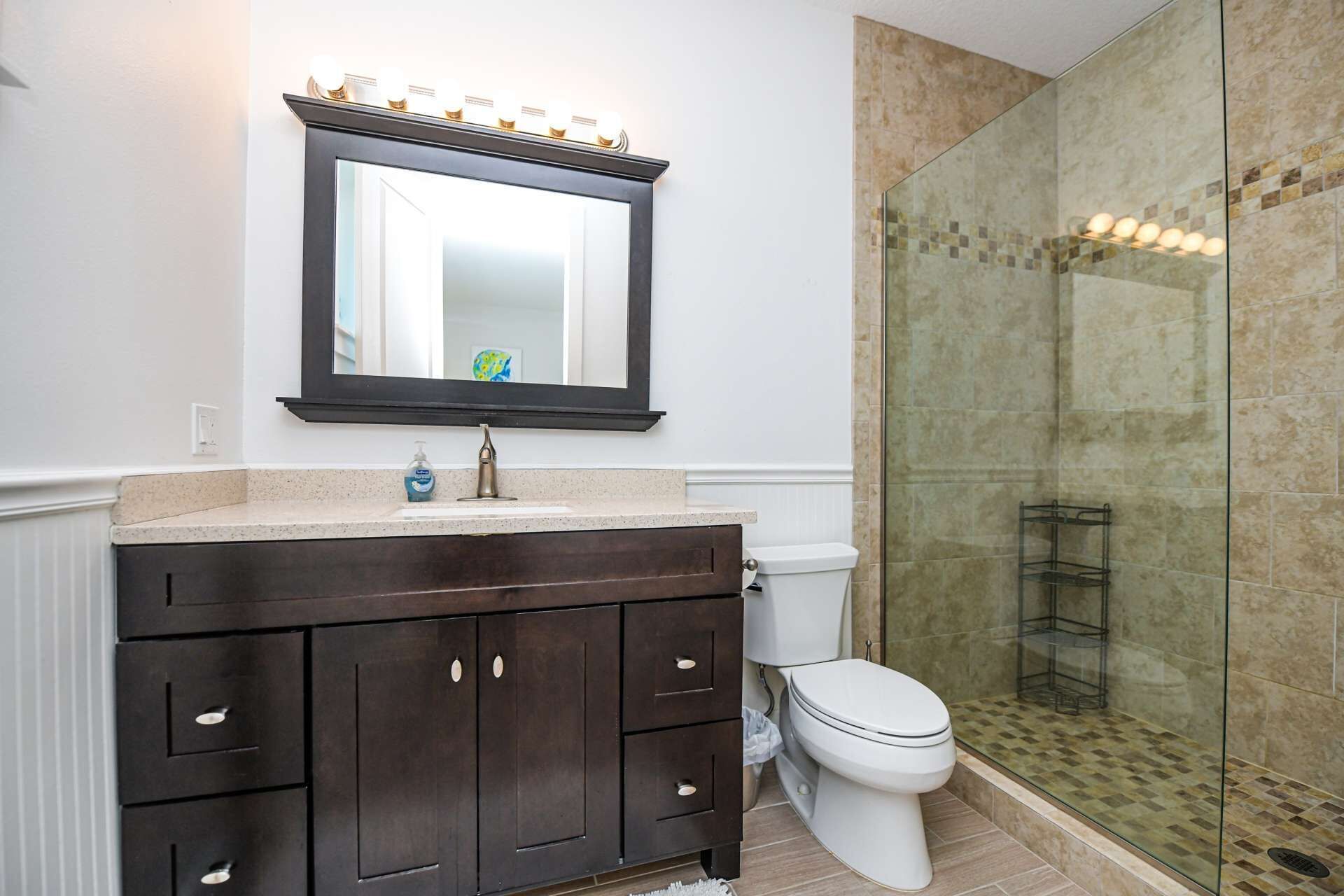 Un baño con tocador de madera oscura, inodoro blanco y cabina de ducha de vidrio.