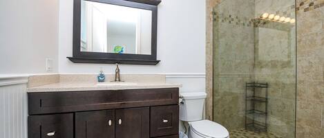 Un baño con tocador de madera oscura, inodoro blanco y cabina de ducha de vidrio.