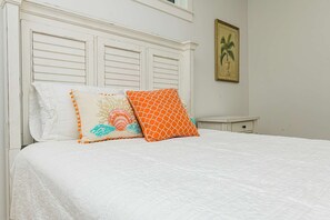 A bed with white bedding and two decorative pillows, a small bedside table, and a framed picture on the wall.