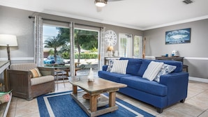 A living room with a blue sofa, a wooden coffee table, and a lamp. There is a large clock on the wall and a poster on the wall. - Minorga Sand Dollar on the Key (Siesta Key)