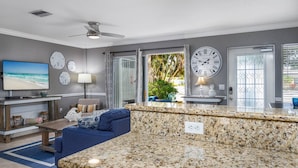 A modern living room with a TV, seating, and a kitchen area with granite countertops. - Minorga Sand Dollar on the Key (Siesta Key)