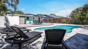 En baghave med swimmingpool, liggestole og en overdækket patio.