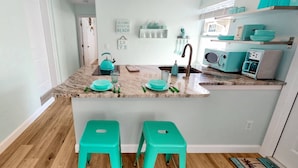 A kitchen with a marble countertop, a sink, two green stools, and teal-colored appliances. - Modern Grove Duplex Unit B (Sarasota)