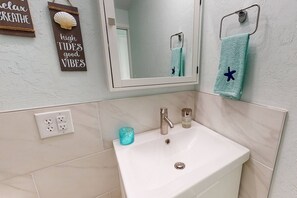 A bathroom with a white sink, a mirror, and a towel rack with a starfish towel. There are two small bottles on the sink and a sign on the wall that says "high tides good vibes." - Modern Grove Duplex Unit B (Sarasota)