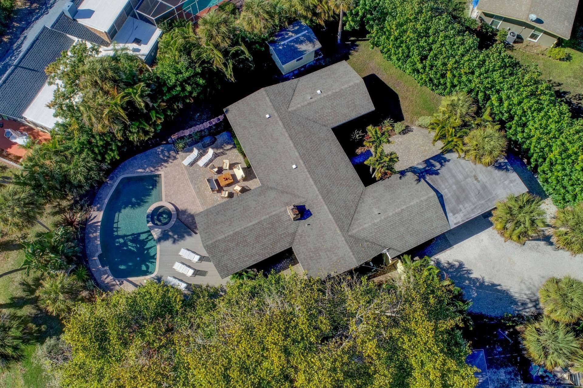 Eine Vogelperspektive auf ein Haus mit Swimmingpool, Terrassenmöbeln und üppiger Vegetation.