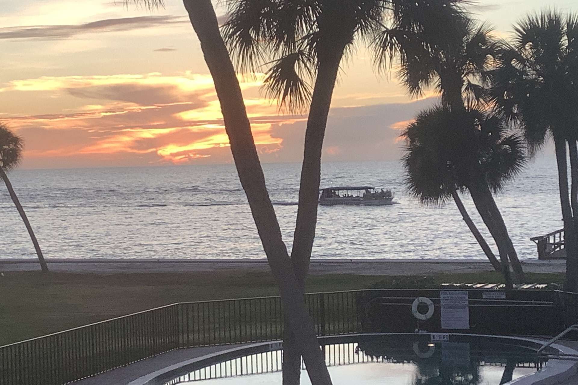 Une vue sur le coucher de soleil, avec des palmiers et un bateau sur l’eau.