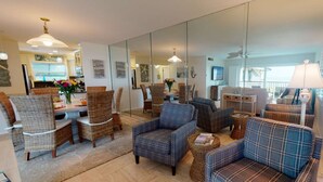 A spacious living area with wicker furniture, a blue plaid sofa, and a dining table with chairs. - Sea Village Gulf Views 2nd Floor Condo (Siesta Key)