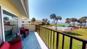 A balcony with a view of the ocean, a pool, and palm trees. - Sea Village Gulf Views 2nd Floor Condo (Siesta Key)