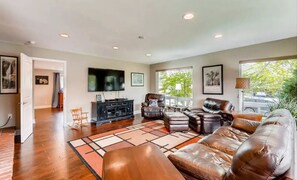 A spacious living room with a leather sofa, a black entertainment unit, and a large window with a view of greenery.