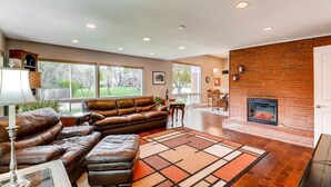 A spacious living room with a leather sectional sofa, a fireplace, and large windows offering a view of the outdoors. - Mid-Century 3 Bdr Lakewood Home Mountain Access! (Lakewood)