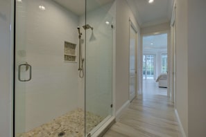 Un baño moderno con cabina de ducha de vidrio, paredes con azulejos blancos y suelo de madera.