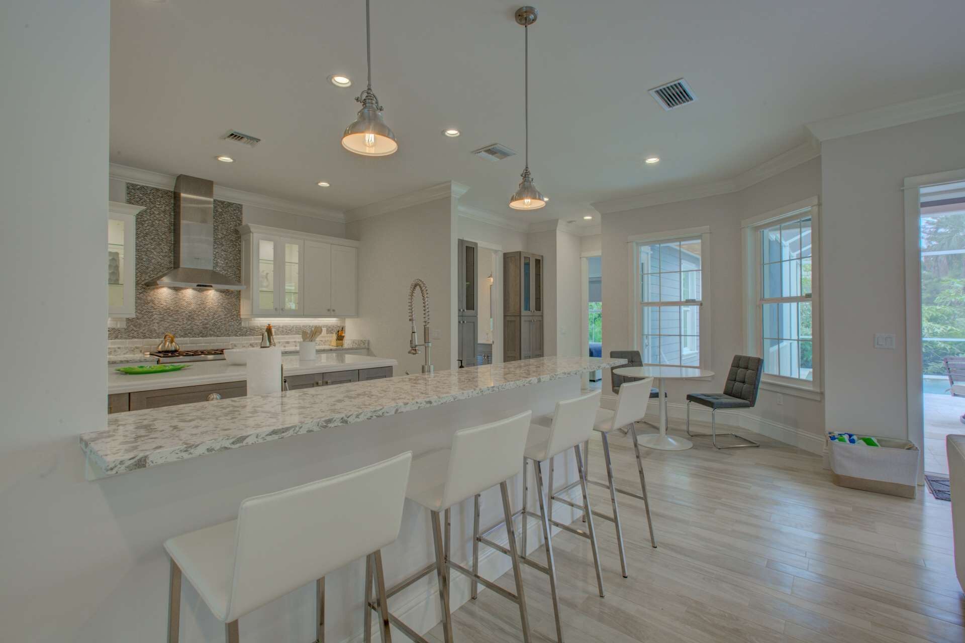 A modern kitchen with marble countertops, white bar stools, and pendant lighting.