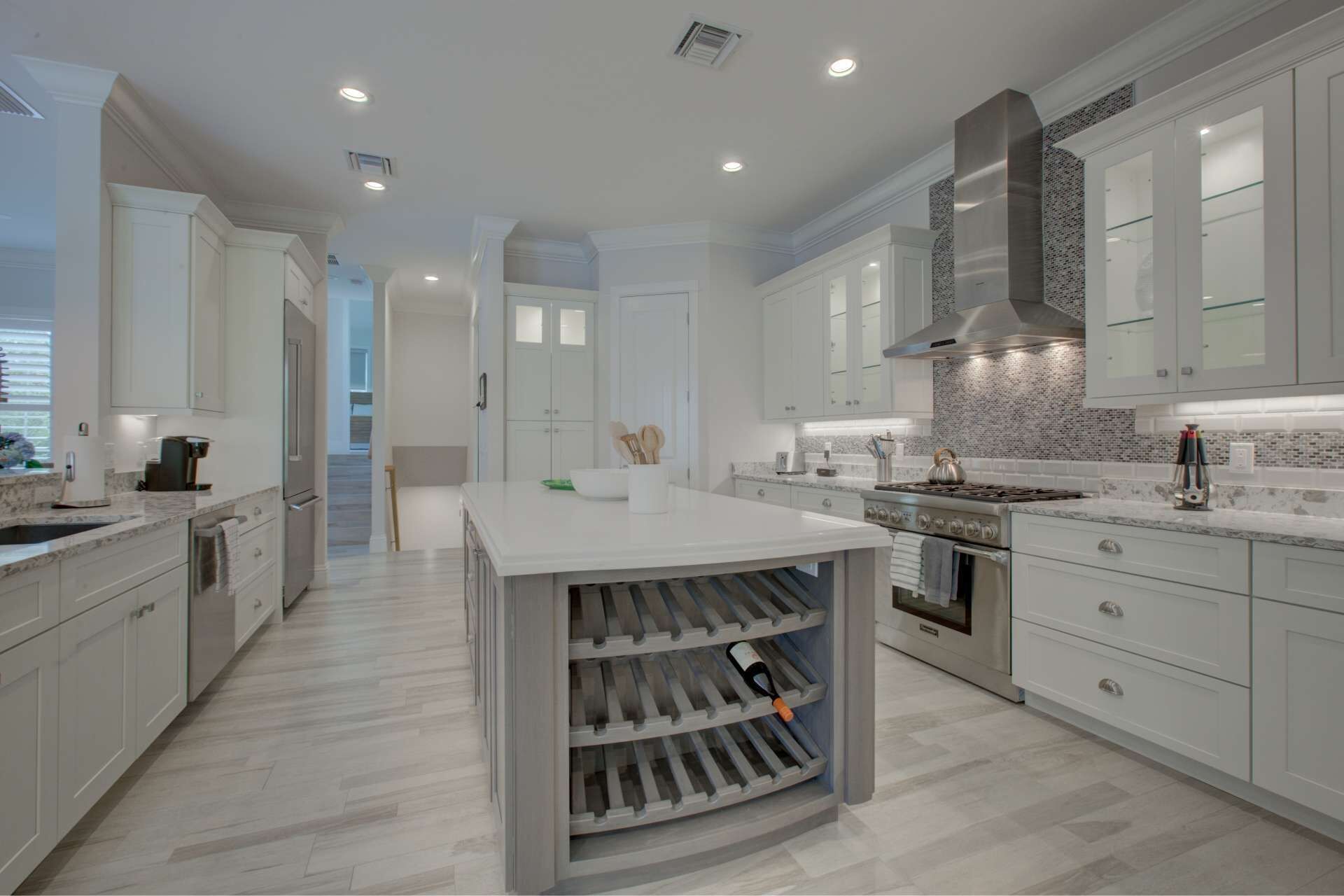 A modern kitchen with white cabinetry, a central island, a built-in wine cooler, and a stainless steel range hood.