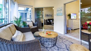 A modern living room with wicker furniture, a round coffee table with a watermelon slice, and a view of the beach through large sliding glass doors. - Siesta Bayside Condo 3 Bedroom (Siesta Key)