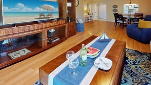 Una sala de estar con una mesa de centro de madera, un televisor, un comedor con una mesa y sillas, y una cocina al fondo.