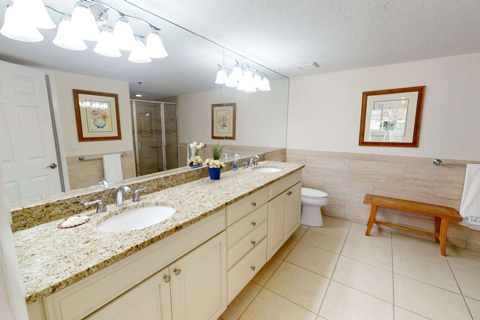 A bathroom with two sinks, a shower, a toilet, and a bench.