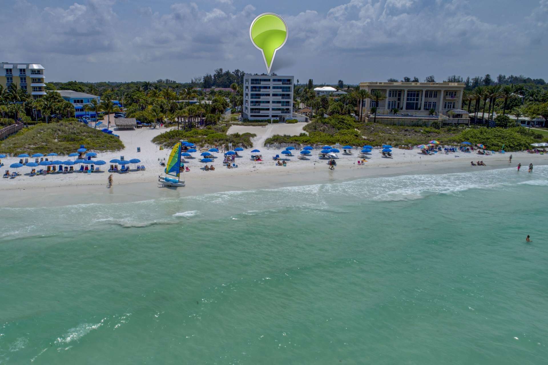 A beach with a sailboat, umbrellas, and buildings in the background.