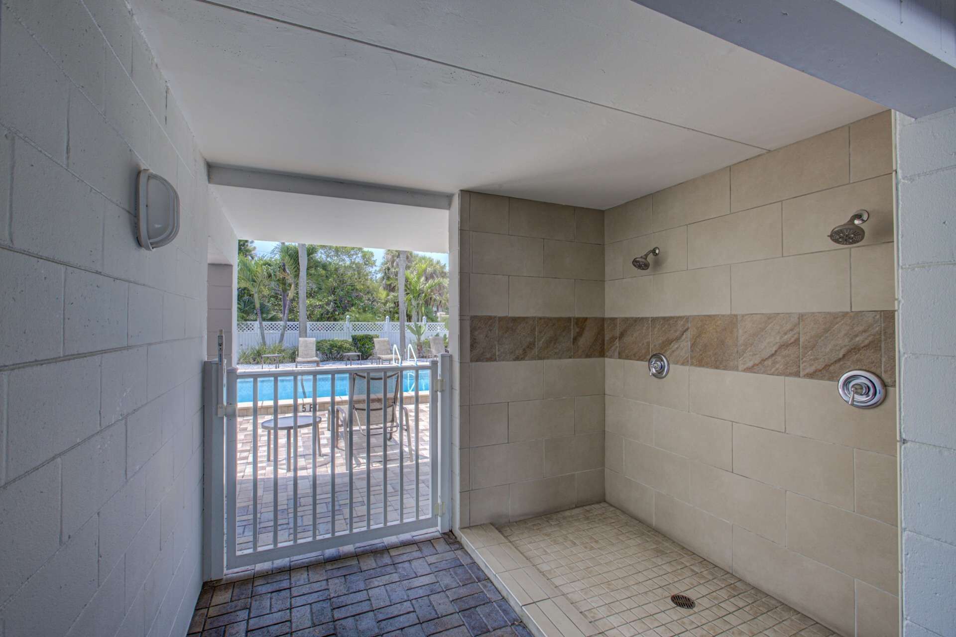 A small, enclosed shower area with tiled walls and a metal door leading to an outdoor pool area.