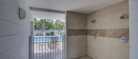 A small, enclosed shower area with tiled walls and a metal door leading to an outdoor pool area.