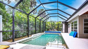 Un área de piscina con agua cristalina, rodeada por un cerramiento de vidrio y exuberante vegetación tropical.