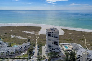 A high-rise hotel with a pool and beach access, surrounded by a parking area and greenery.
