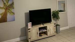 A living room with a flat-screen TV on a wooden cabinet, a small plant, a framed picture, and a ceiling fan. - Cozy getaway! Minutes from Historic Pinellas Trail! (Largo)