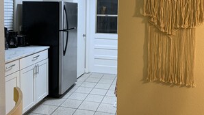 A kitchen with white cabinets, a black refrigerator, and a macrame wall hanging. - Cozy getaway! Minutes from Historic Pinellas Trail! (Largo)