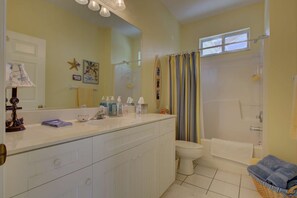 A bathroom with a white vanity, a toilet, a bathtub, and a shower curtain.
