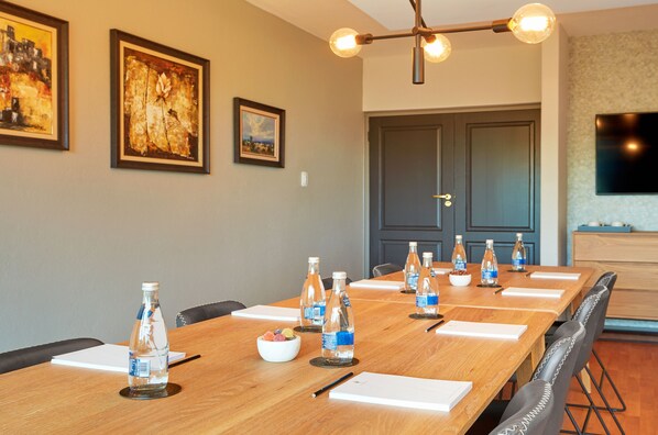 Un salón de conferencias con una larga mesa de madera, botellas de agua y un frutero.