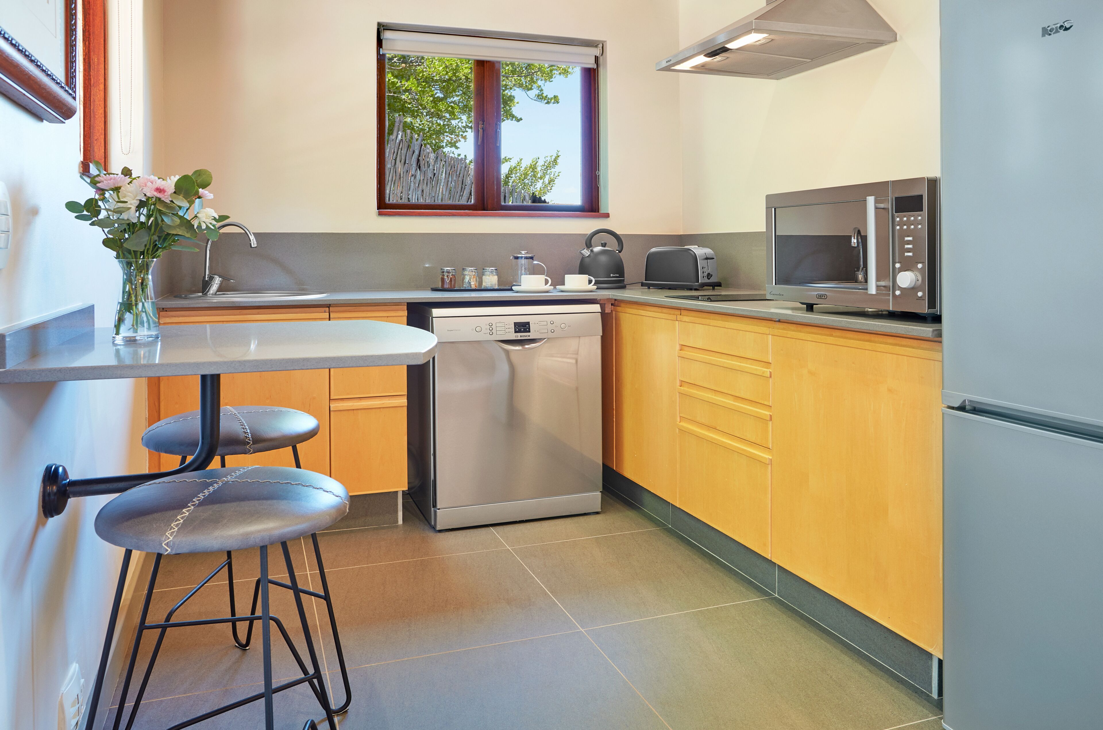 A modern kitchen with a dishwasher, microwave, and a window with a view of trees.