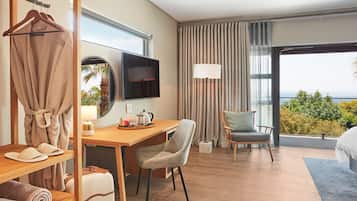 A hotel room with a wooden desk, a chair, a bed, a TV, and a view of the outdoors.