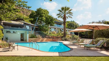 Una piscina al aire libre, sombrillas, sillones reclinables de piscina