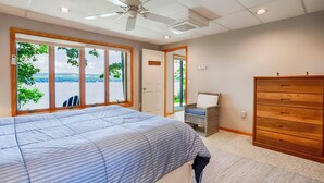 A bedroom with a large bed, a dresser, and a view of the lake.
