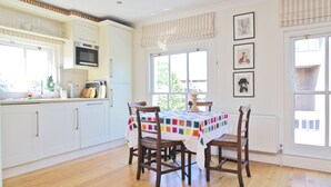 A kitchen with white cabinets, a microwave, a table with a colorful tablecloth, and wooden chairs.