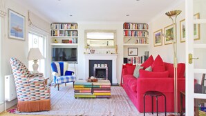A living room with a fireplace, bookshelves, a red sofa, and a patterned armchair.