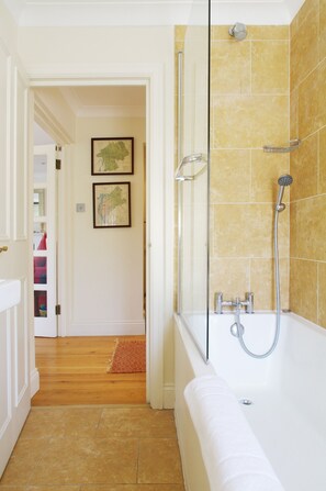Ein Badezimmer mit Badewanne, Dusche und einem Flur, der zu einem Raum mit einer Tür führt.